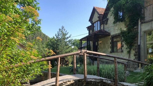 A stone bridge over a pond with a house in the background. - Eco Garden Dilijan (Dilijan)