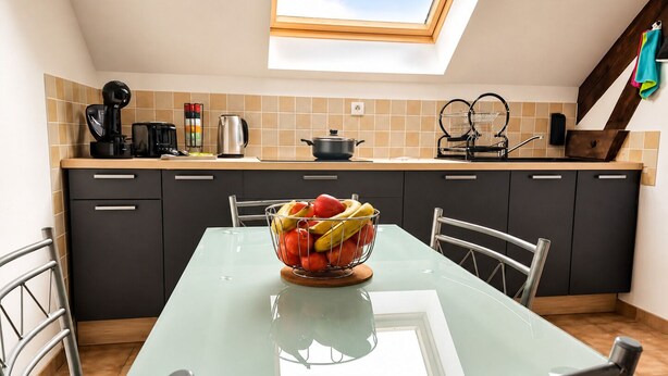Una cocina moderna con tragaluz, una mesa de comedor con sillas y un frutero sobre la mesa.