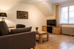 Uma sala de estar com sofá, mesa de centro, TV sobre um armário de madeira, radiador e janela com cortinas.