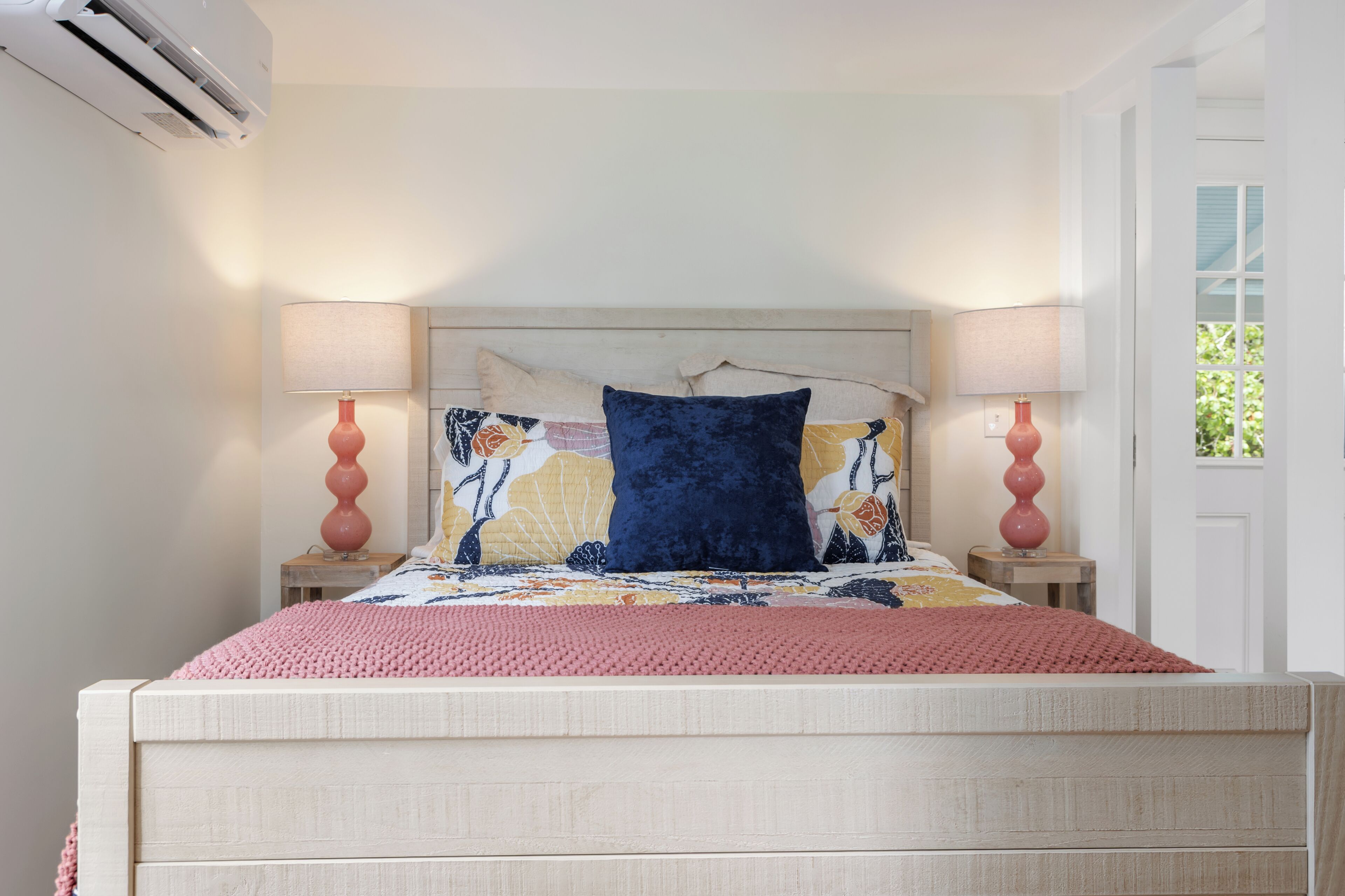 Un dormitorio con cama, dos lámparas de noche, una ventana y un aire acondicionado.