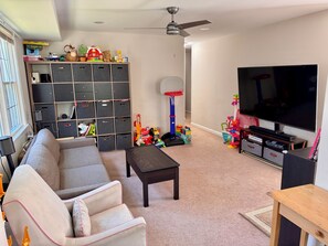 A living room with a sofa, a coffee table, a television, a bookshelf, and a basketball hoop. - Old Town House w Driveway & Backyard • 3 Blocks to King St • Family Friendly (Alexandria)