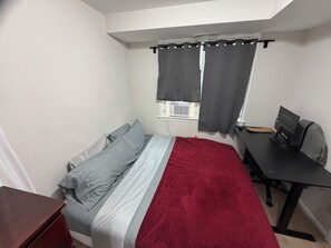 Un dormitorio con cama, escritorio, silla y ventana con cortinas.
