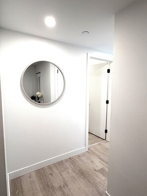 A hallway with a round mirror, white walls, and a wooden floor. - 2 Bedroom Lakeview in Downtown Kelowna with Rooftop Terrace + EV Parking (Kelowna)