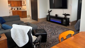 Un soggiorno con divano, poggiapiedi, televisione, mobile TV e zona pranzo con tavolo e sedie.