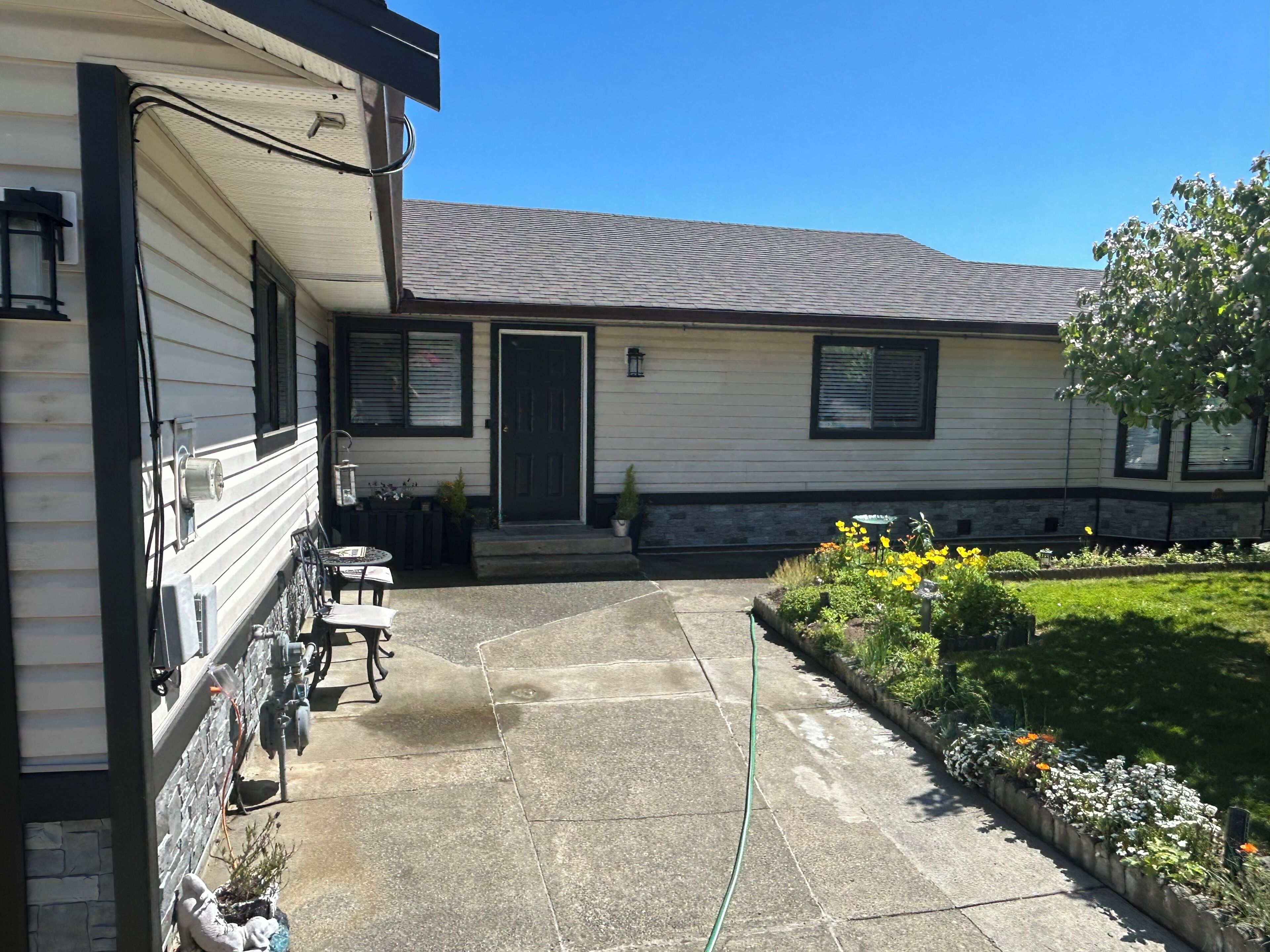 A residential building with a covered patio, outdoor seating, and a garden with flowers.