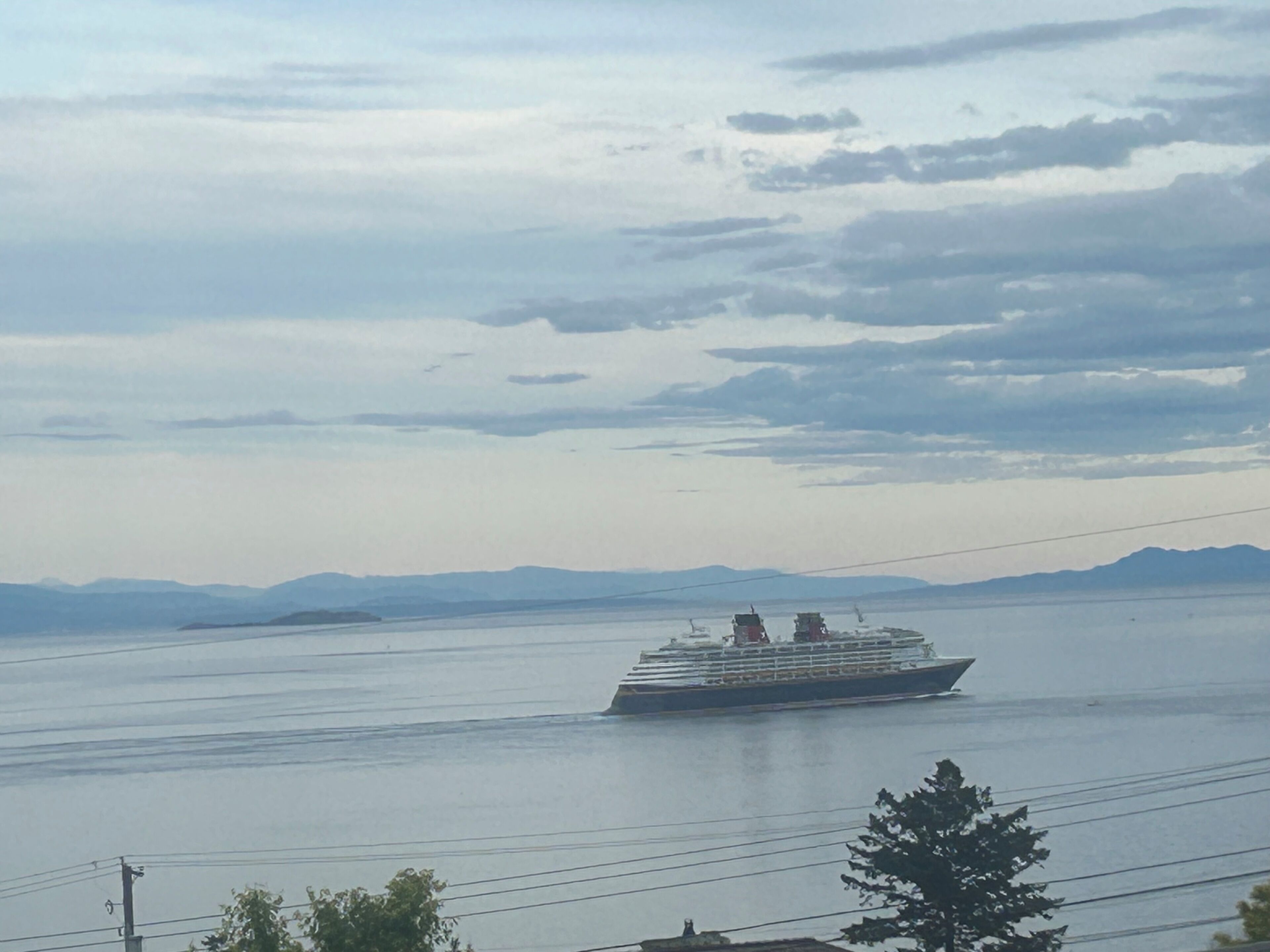 A cruise ship on a calm body of water with distant mountains and a cloudy sky.