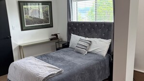 Una camera da letto con un letto, un comodino, un quadro incorniciato e una finestra con tende.