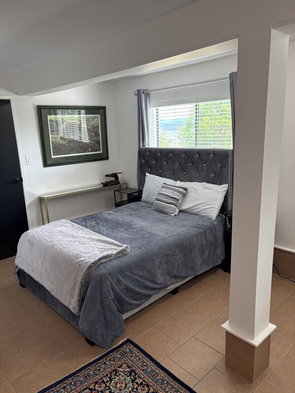 A bedroom with a bed, a nightstand, a framed picture, and a window with curtains. - Campbell River discovery passage view guest suite (Campbell River)