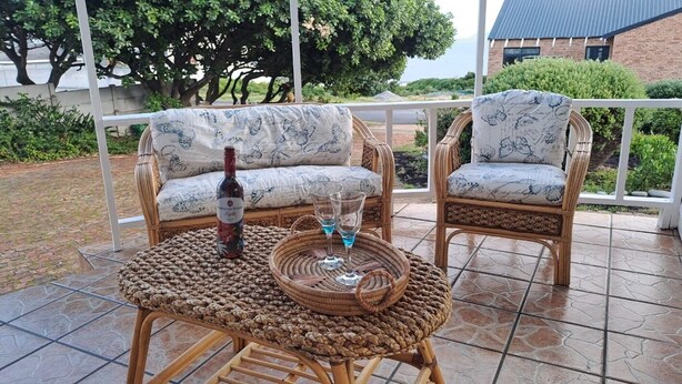 Une table en osier avec une bouteille et des verres, deux chaises en osier et un banc rembourré à motifs floraux.