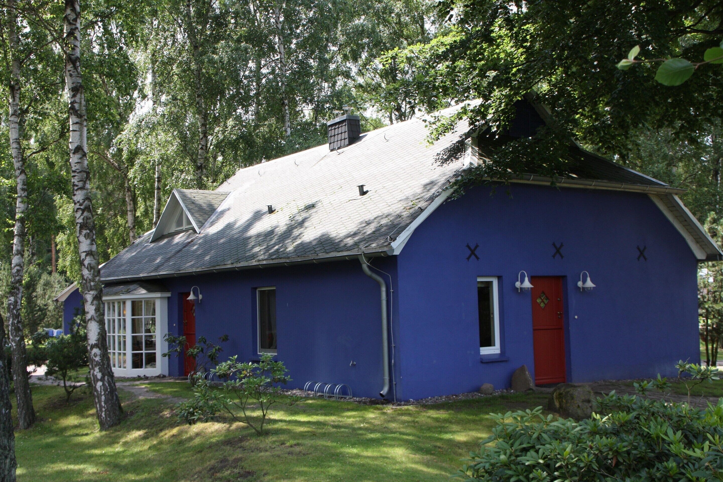 A blue house with a red door, surrounded by trees and greenery.