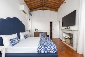 A bedroom with a bed, bedside tables, a desk, a fireplace, and a TV.