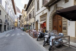 A narrow street lined with historic buildings, a parked scooter, and a café with outdoor seating.