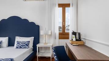 A hotel room with a bed, bedside table, lamp, desk, chair, and a window with a view.