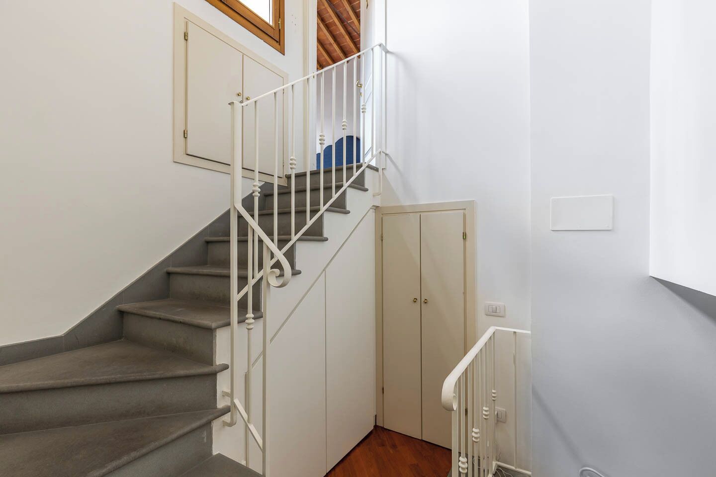 A staircase with a white railing, a wooden door, and a light switch on the wall.