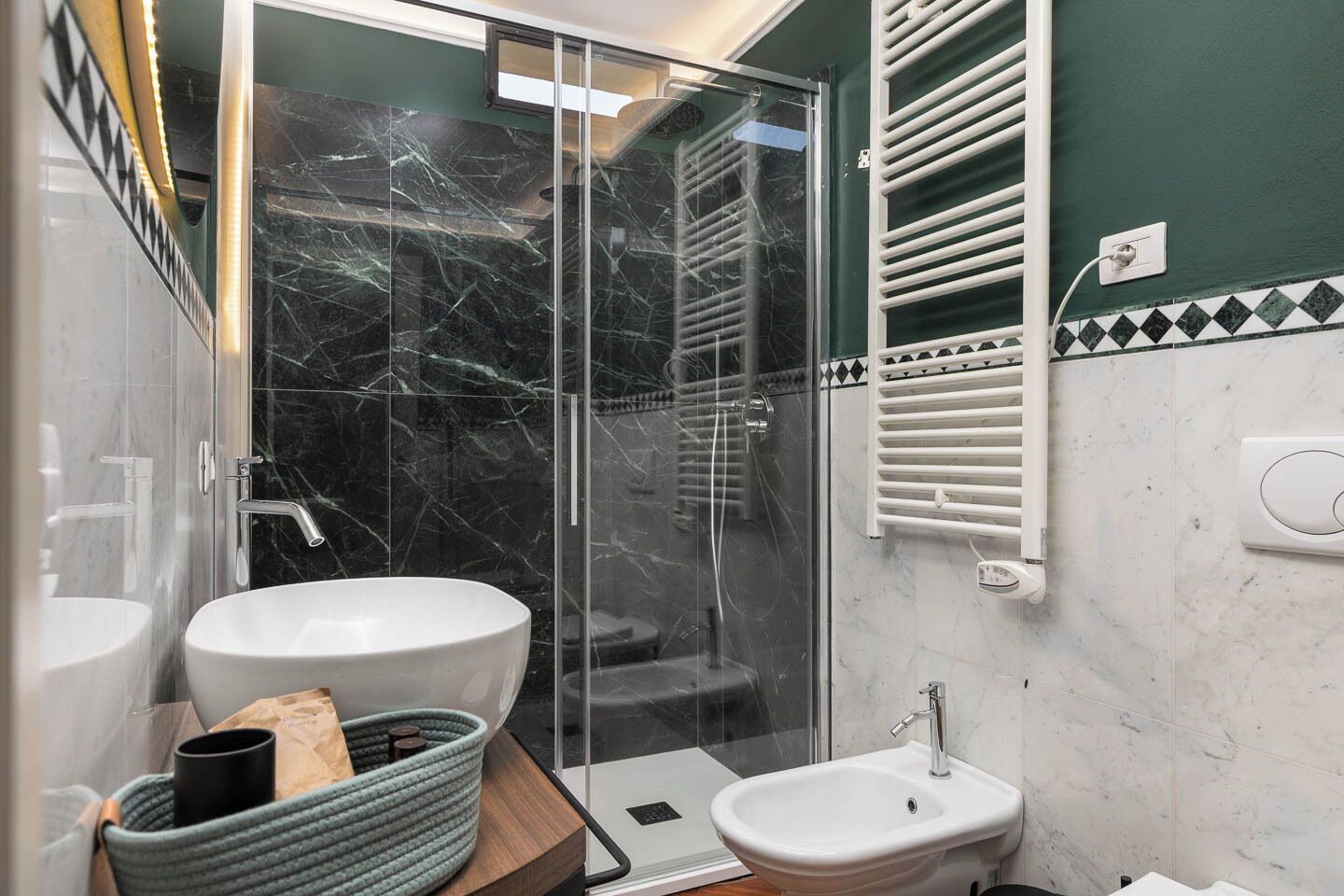 A bathroom with a glass shower enclosure, a white sink, a bidet, and a towel rack.