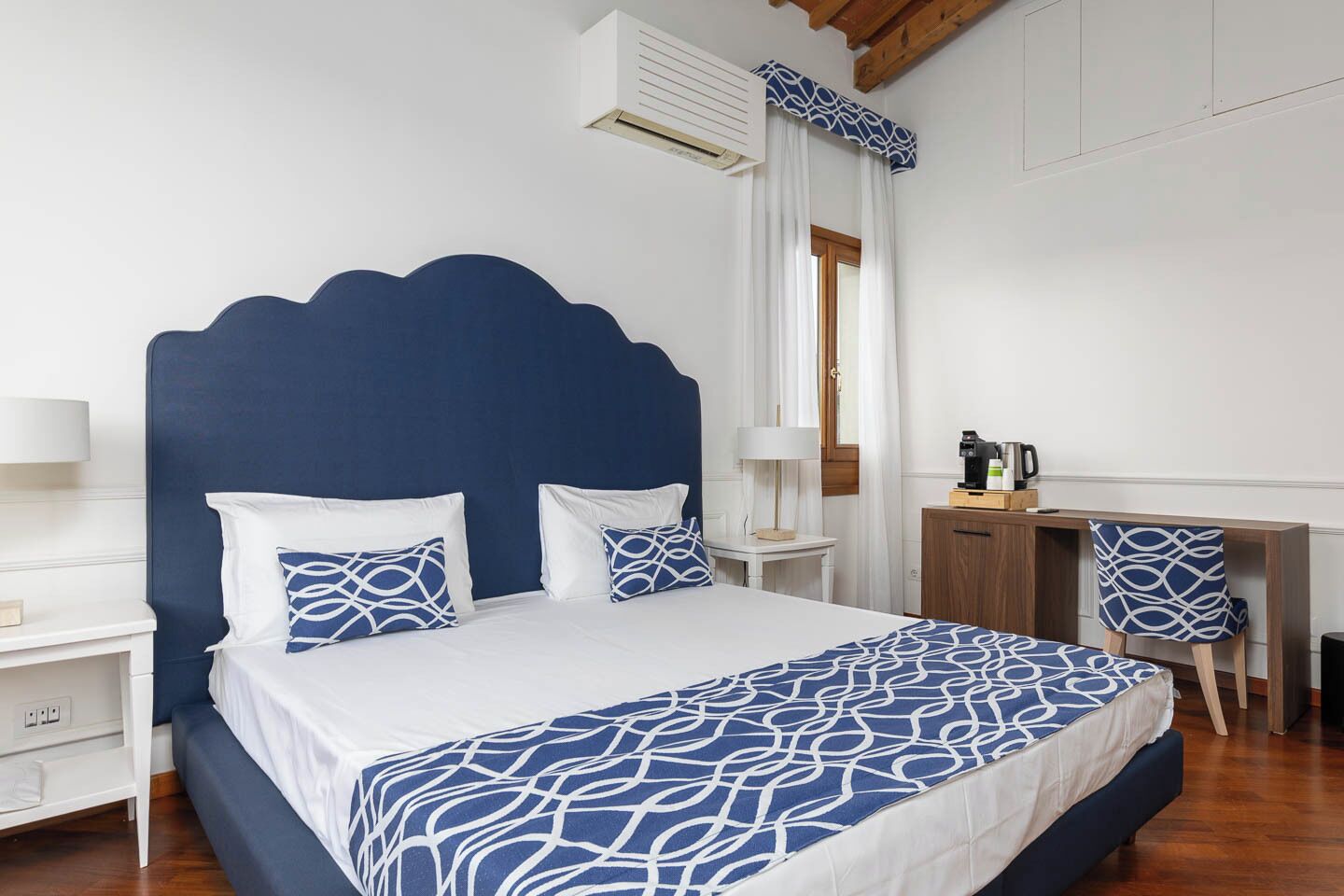 A bedroom with a large bed, a desk, a chair, and a window with curtains.