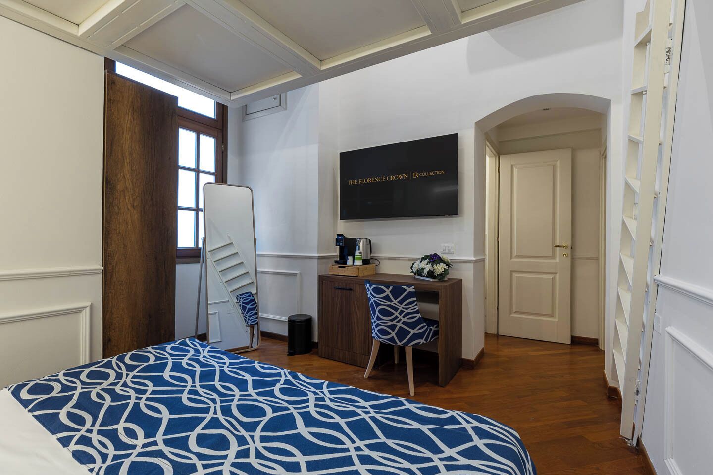 A bedroom with a bed, a desk, a chair, a TV, and a door.