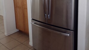 Ein Edelstahl-Kühlschrank in einer Küche mit Holzschränken und Fliesenboden.