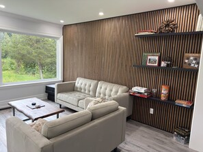 Ein modernes Wohnzimmer mit einem Ecksofa, einer Holz-Akzentwand und einem Bücherregal mit Gesellschaftsspielen.