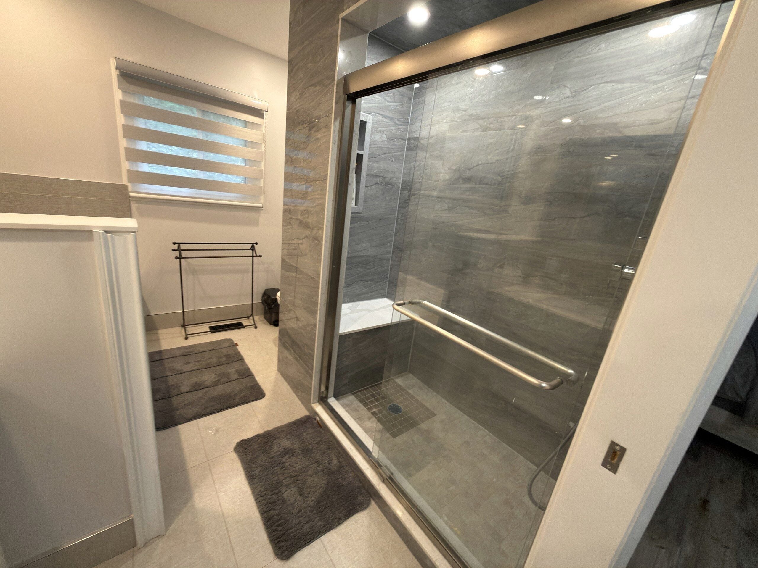 Une salle de bain moderne avec une douche à parois de verre, un porte-serviettes et un petit tapis sur le sol.