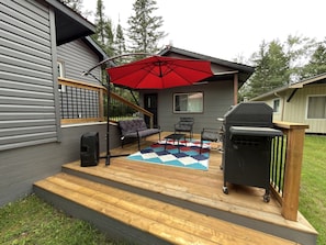 A deck with a grill, outdoor furniture, and a red umbrella. - Modern Pigeon Lake Waterfront Cottage | 3BR + Fireplace (Bobcaygeon)