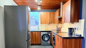 Eine kleine Küche mit Holzausstattung, einer Waschmaschine, einer Kaffeemaschine und einem Mülleimer.