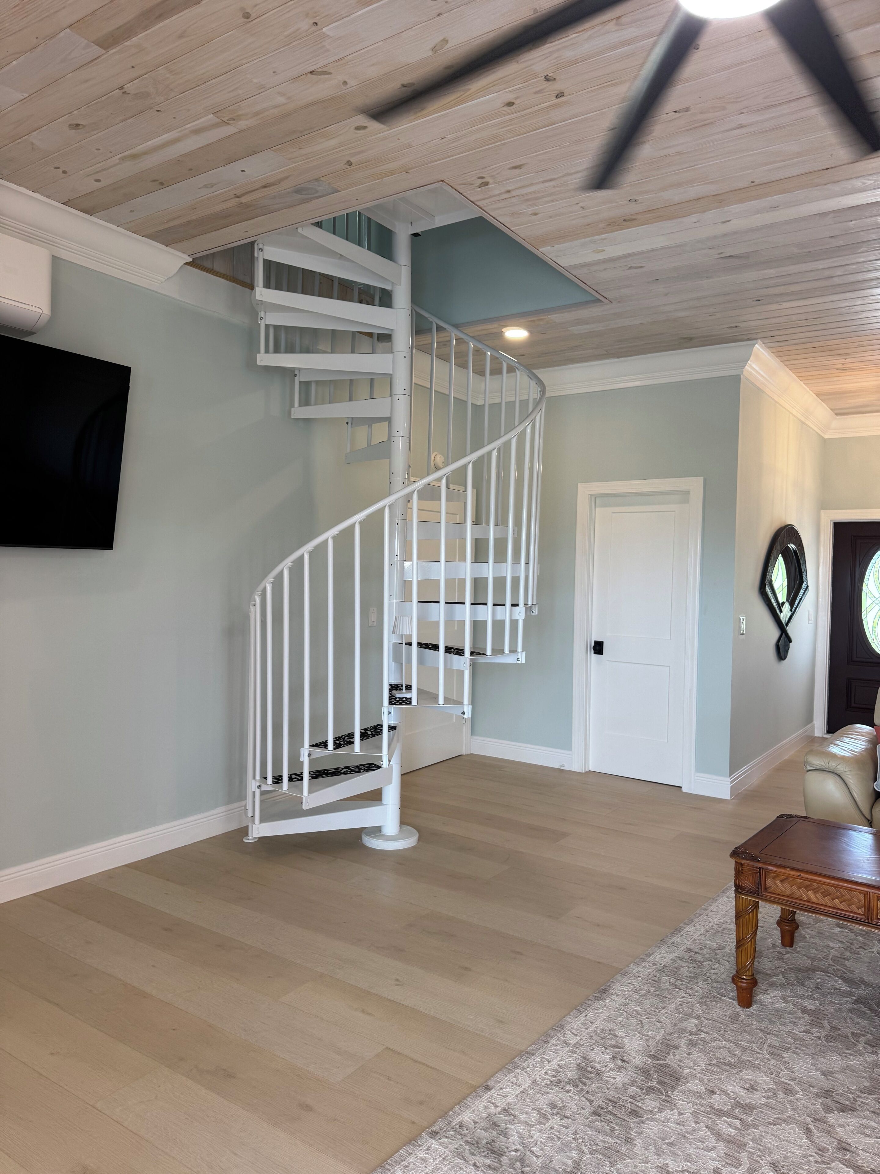 A modern interior with a spiral staircase, a flat-screen TV, and a leather sofa.