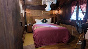 A wooden room with a bed, a nightstand, a fan, and a window with curtains. - Step Back in Time at L’Auberge de Meo Vac: A Century-Old H’mong Estate (Meo Vac)
