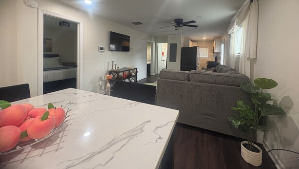 A modern living room with a sofa, a dining table with a fruit bowl, a ceiling fan, and a kitchen area in the background. - Modern Family Friendly Atlanta] Home - 4 miles to Mercedes-Benz Stadium (Atlanta)