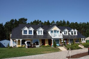Ein zweigeschossiges Haus mit Balkon, überdachter Veranda und kleinem Garten.