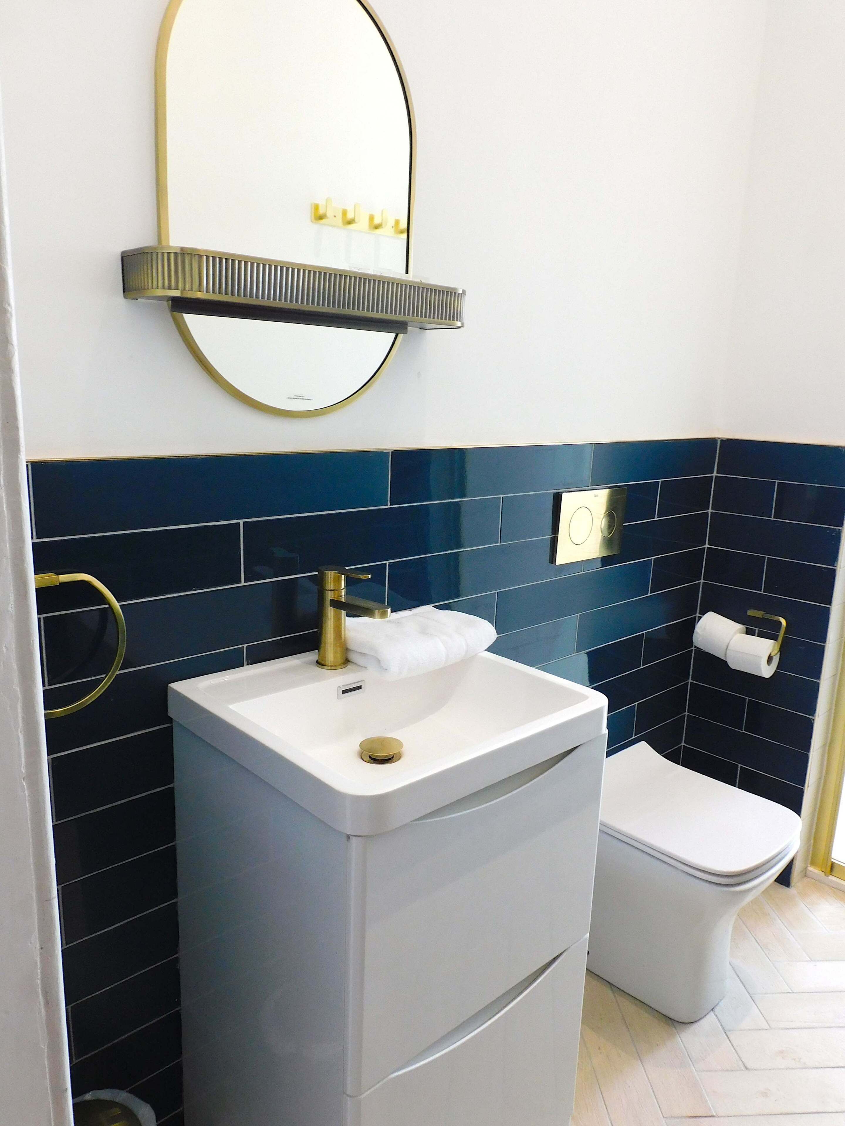 Et badeværelse med en hvid vask, et toilet og et spejl med gylden ramme.