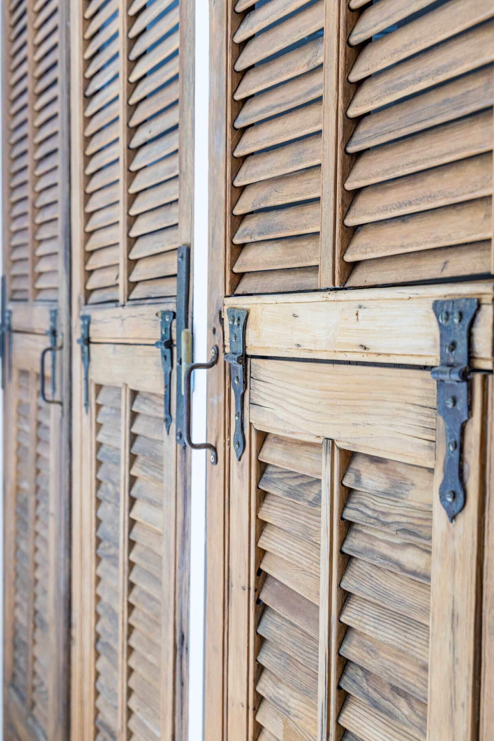 A row of wooden shutters with metal hinges and latches.
