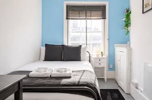 Quarto com cama, mesa de cabeceira, abajur e vista pela janela.