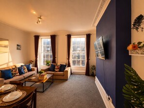 Ein Wohnzimmer mit einer Couch, einem Couchtisch und einem an der Wand befestigten Fernseher.