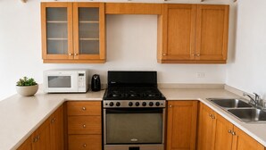 A kitchen with wooden cabinets, a microwave, a stove, and a sink. - 2BR Garden Suite – Minutes from a Glowing Lagoon (Falmouth)