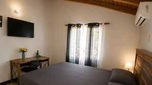 A bedroom with a bed, a desk, a chair, a TV, and an air conditioner. - 2BR Garden Suite – Minutes from a Glowing Lagoon (Falmouth)