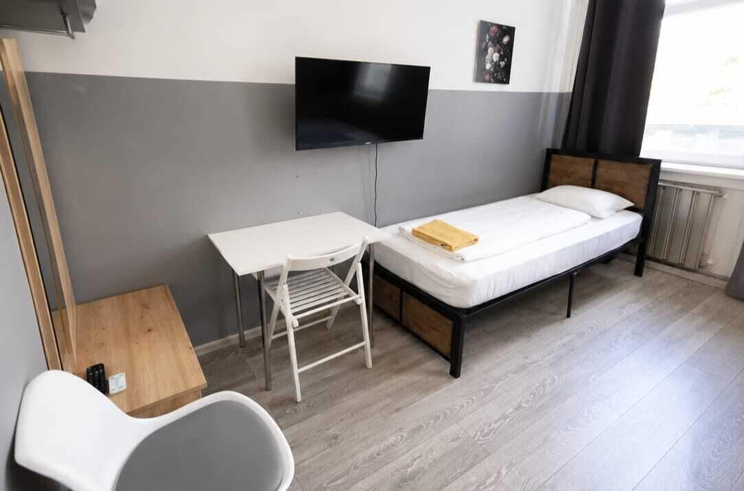 A small, modern room with a single bed, a desk, and a TV mounted on the wall.