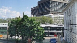 Un edificio moderno con fachada de vidrio, un árbol en primer plano y un cielo despejado.