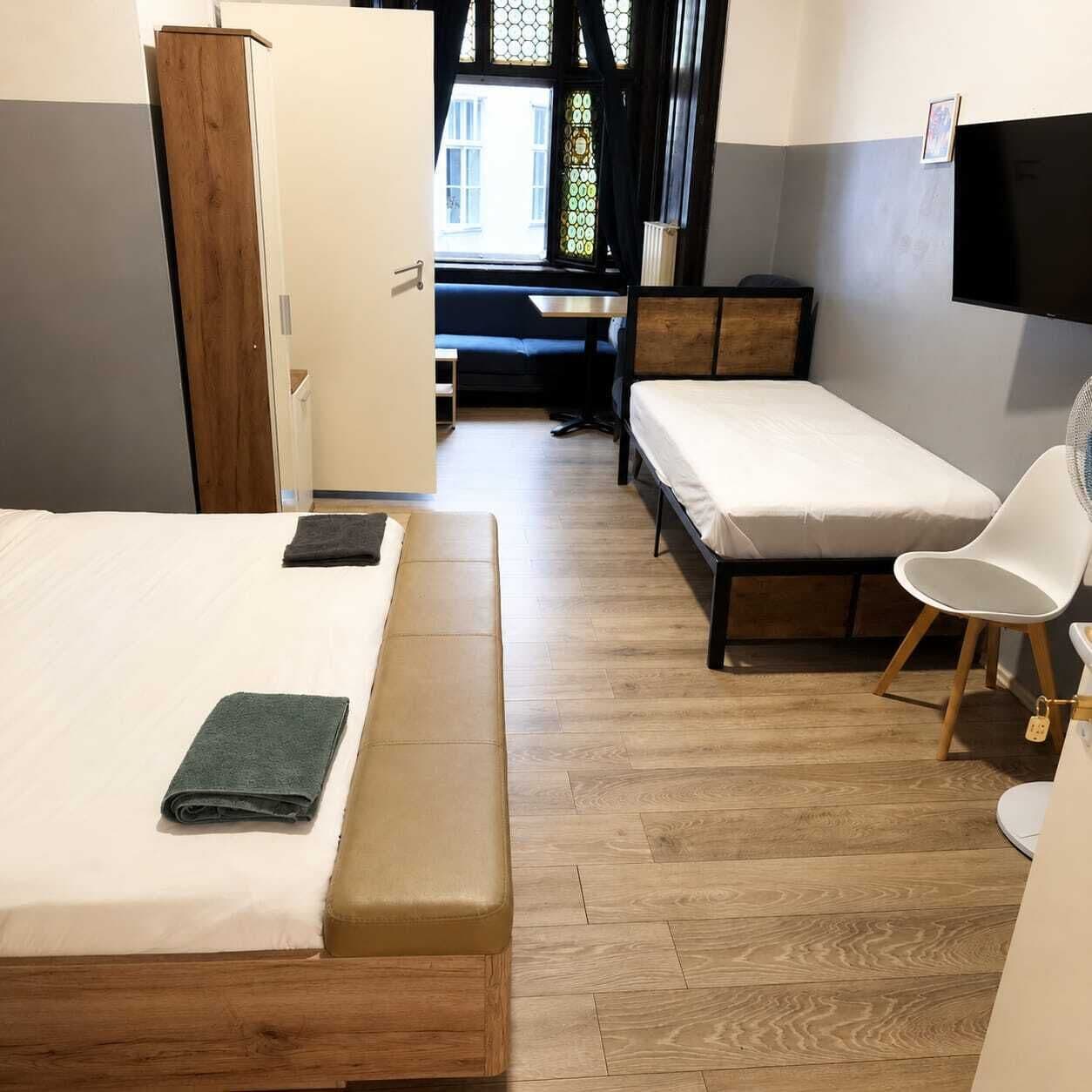 Ein Zimmer mit zwei Betten, einem Schreibtisch, einem Stuhl und einem Fernseher.