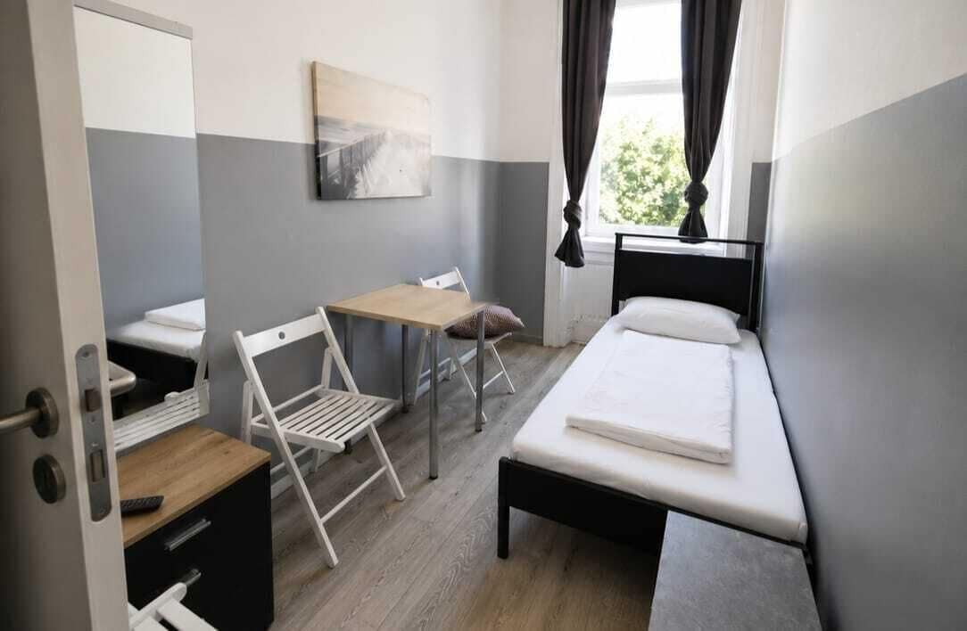 Ein kleines Hotelzimmer mit einem Bett, einem Schreibtisch, einem Sessel und einem kleinen Tisch.
