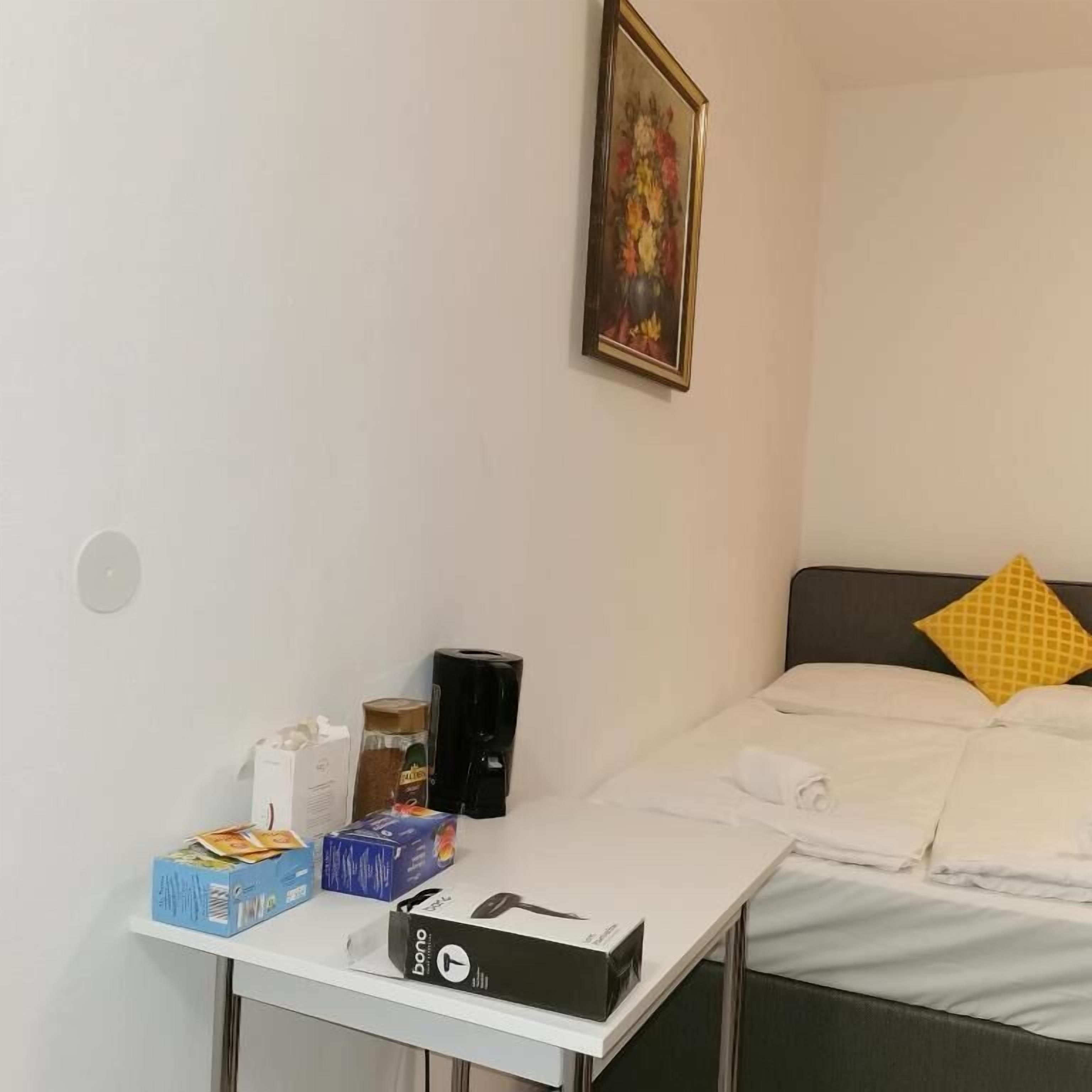 Una habitación de hotel con una cama, una mesita con cajas, una cafetera y un cuadro en la pared.