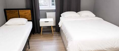 A room with two single beds, a small white chair, and a window with curtains.