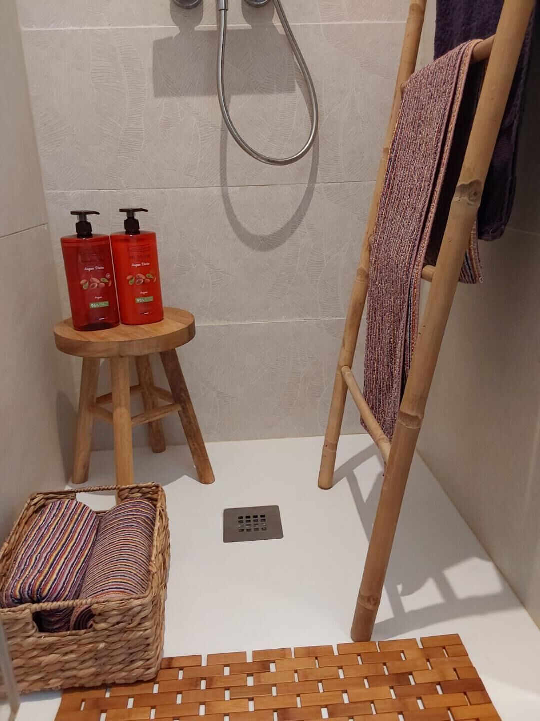 A shower area with a wooden stool, a towel rack, and a woven basket.