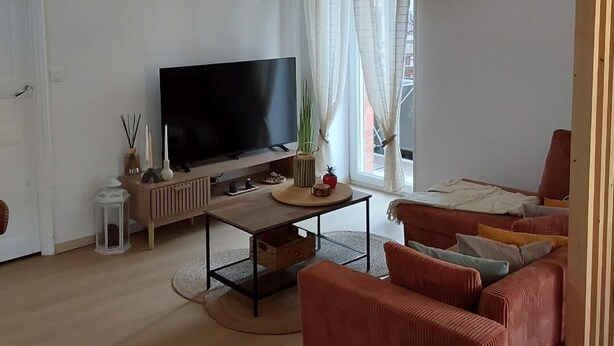 A living room with a flat-screen TV, a sofa, a coffee table, and a window with curtains.