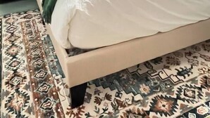 Una cama bien hecha con un plaid verde, una alfombra estampada y una mesita de noche con lámpara.