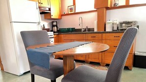 Una cocina con mesa y dos sillas, armarios de madera, un refrigerador y una cafetera.