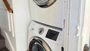 Una lavadora y secadora apiladas en una habitación con una puerta de madera y una escalera.