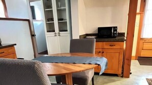 Un comedor con mesa de madera, dos sillas, un aparador con puertas de vidrio y un microondas sobre una encimera.