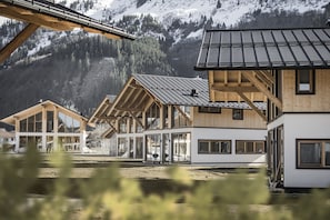 Eine Reihe von Holzhütten mit großen Fenstern und einem Metall-Dach, vor einer Bergkulisse gelegen.