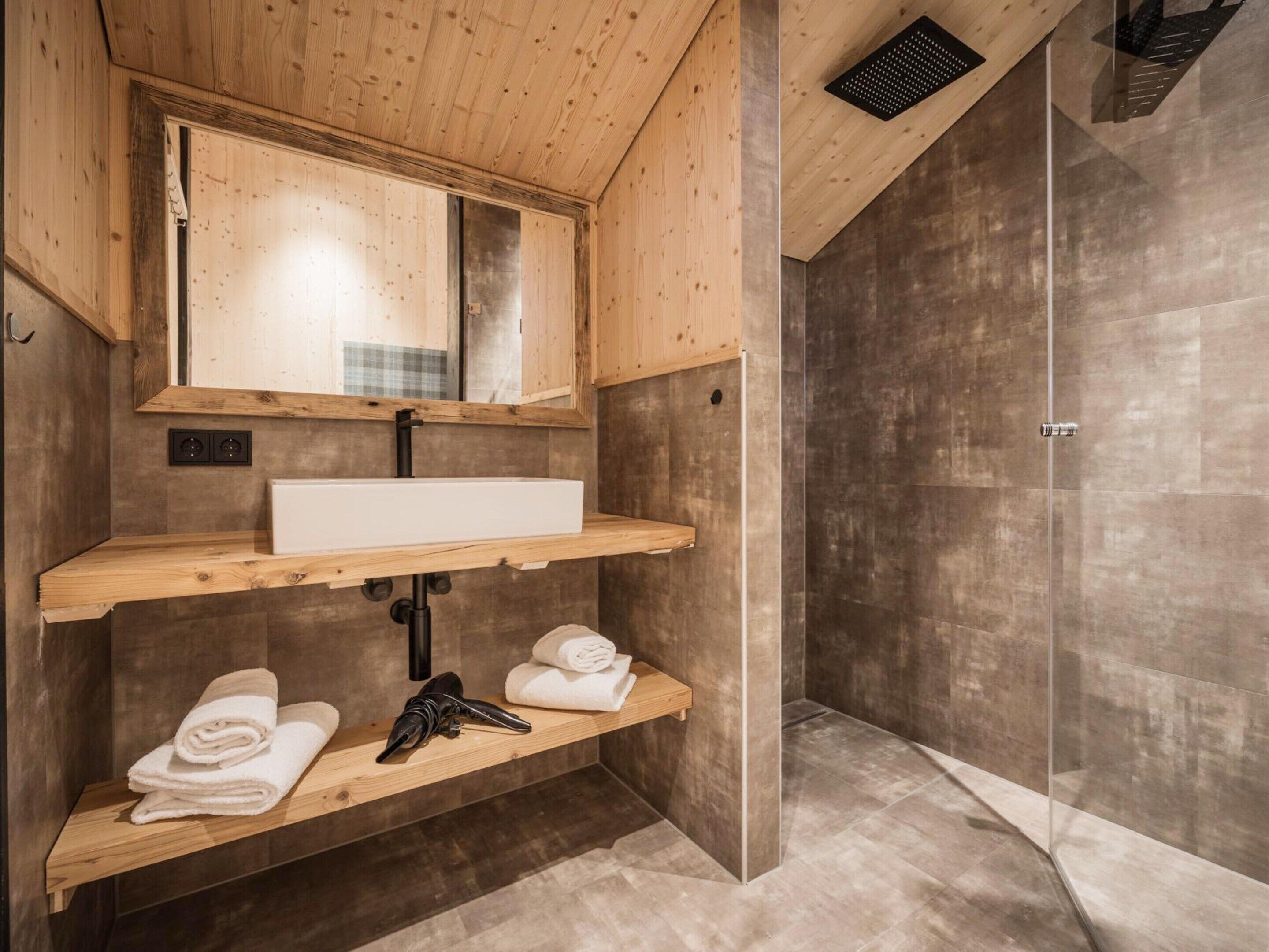 Un baño moderno con tocador de madera, un espejo grande, zona de ducha y un perchero para toallas.